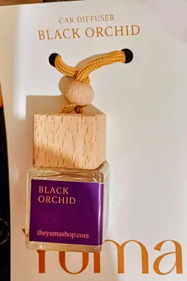 Small glass Black Orchid car fragrance bottle with a wooden stopper and cord on a white background.