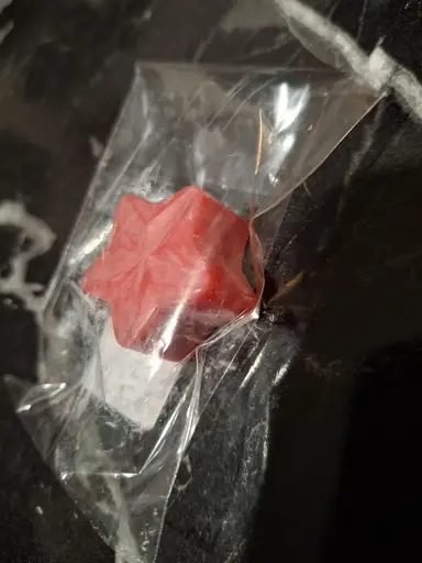 A red star-shaped candle in clear plastic packaging on a dark surface.