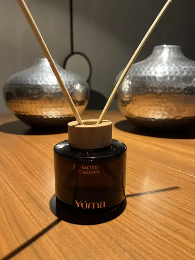 YUMA Salted Caramel reed diffuser with a wooden cap and two reeds on a wooden surface.