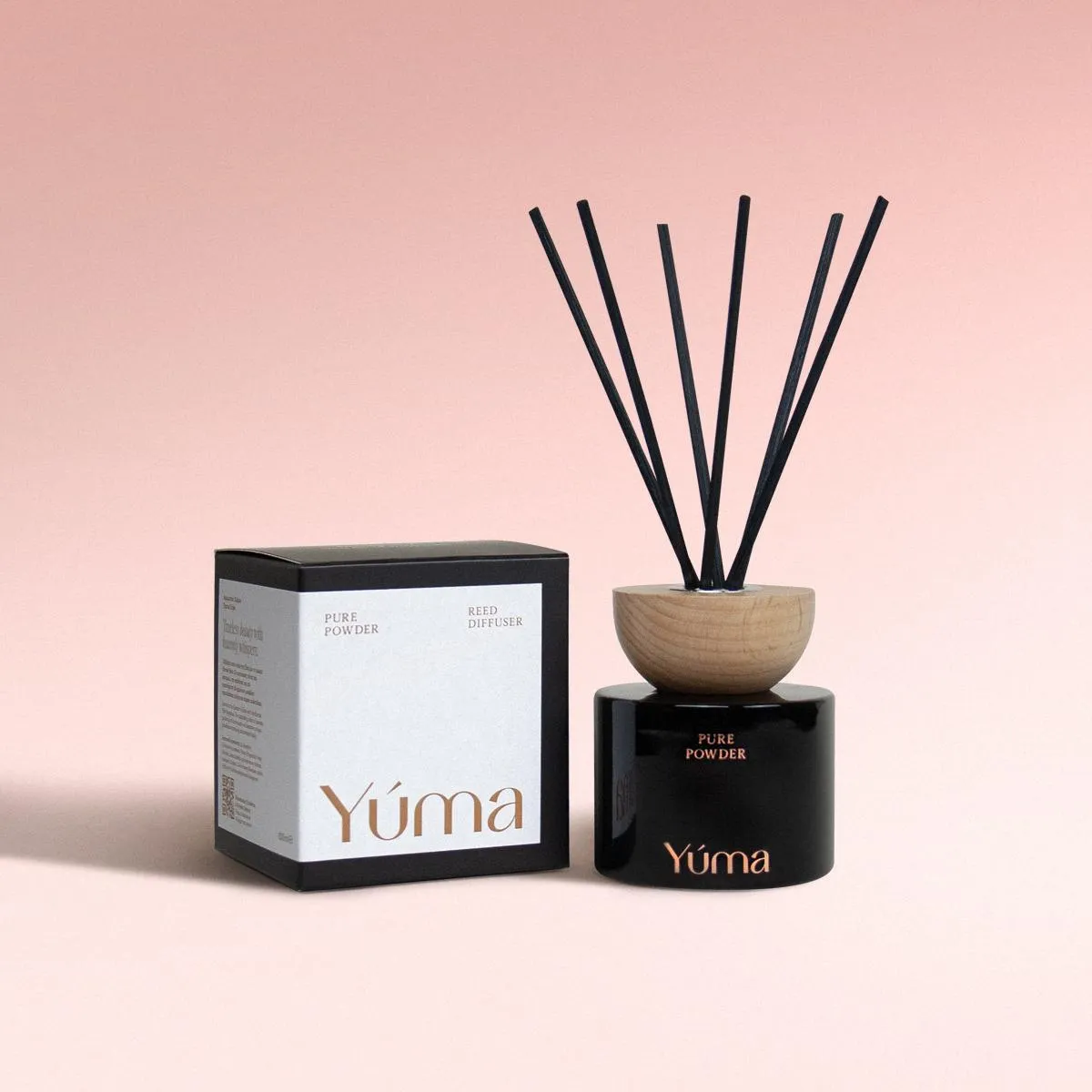 YUMA Pure Powder reed diffuser in a black glass bottle next to its paper packaging.