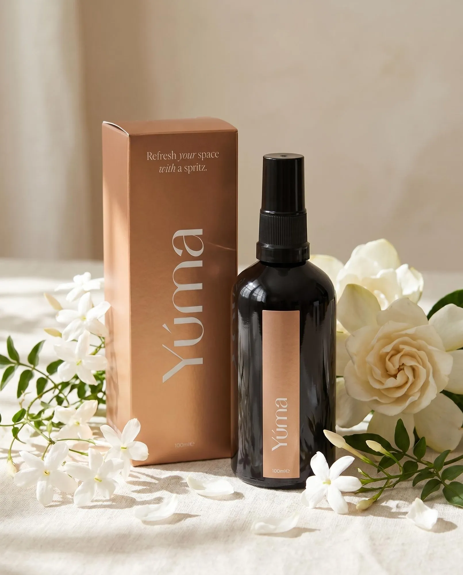 YUMA Eternal Eden black fabric spray bottle next to a copper box and white jasmine flowers.
