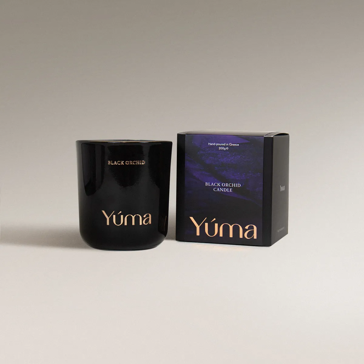 YUMA Black Orchid candle in a black glass vessel beside its paper packaging on a grey background.
