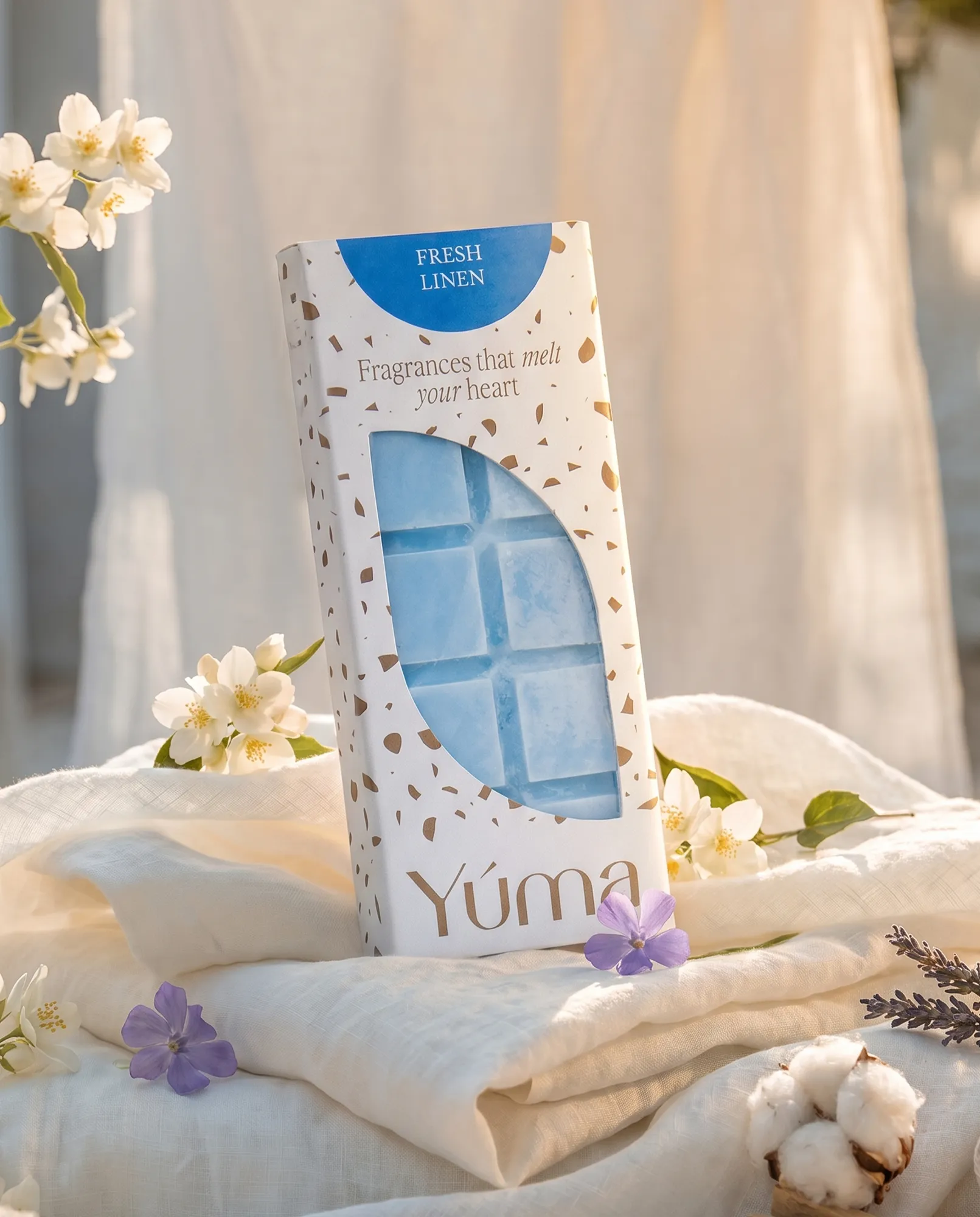 YUMA Fresh Linen blue Wax Melts in white packaging, placed on white fabric with flowers.