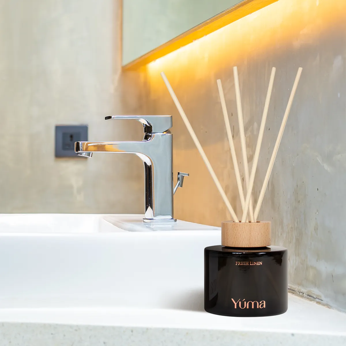 YUMA Amber Tobacco reed diffuser in a black glass vessel, placed beside a bathroom sink.
