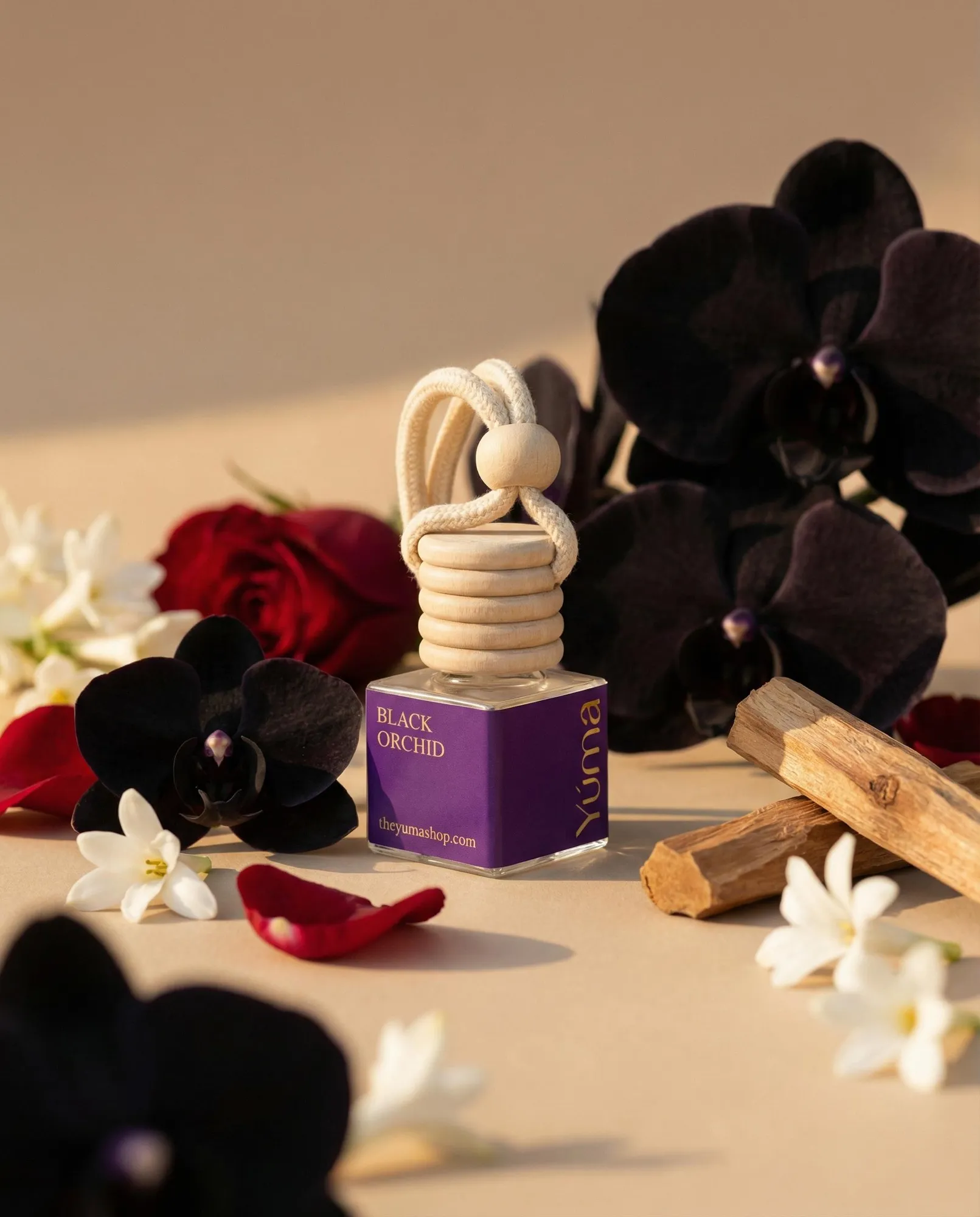YUMA Black Orchid car diffuser surrounded by black orchids, red roses, and wood.