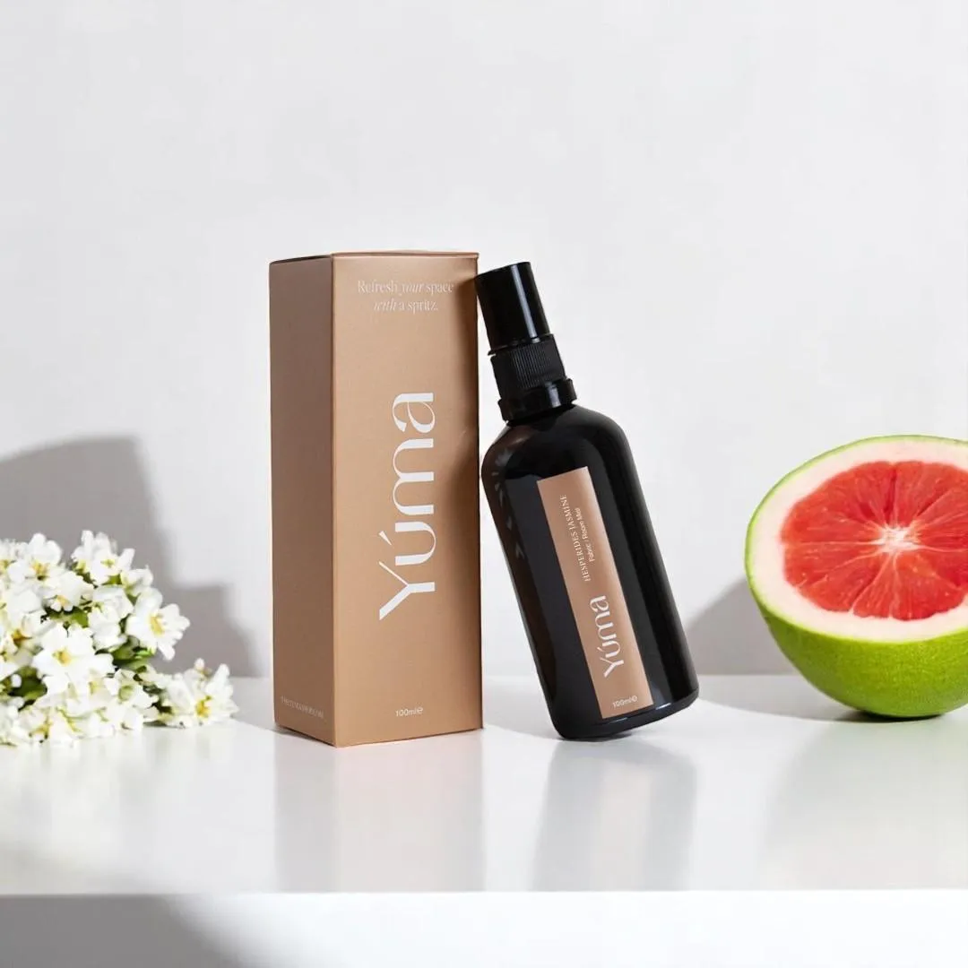 YUMA Hesperides Jasmine room spray next to its packaging, white blossoms, and a halved grapefruit.