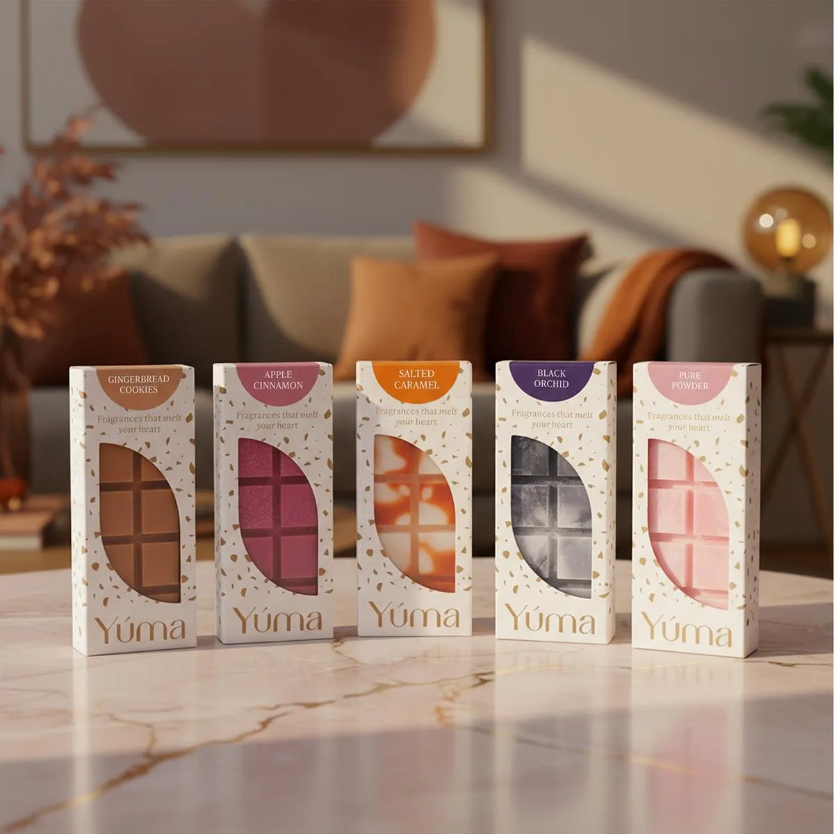 Five assorted YUMA wax melts in white packaging on a marble coffee table.