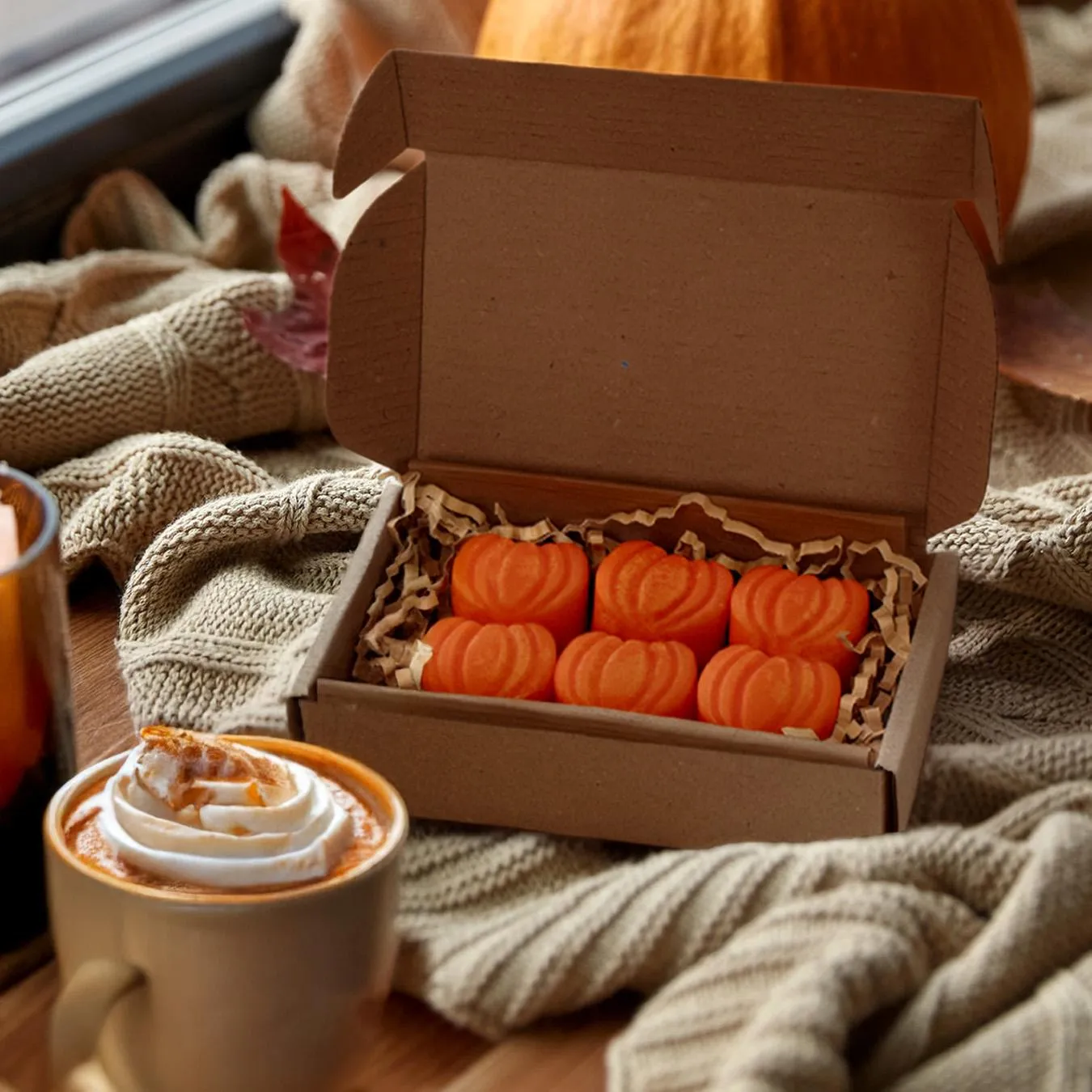 Six orange pumpkin-shaped Pumpkin Pie wax melts in a paper box next to a drink.