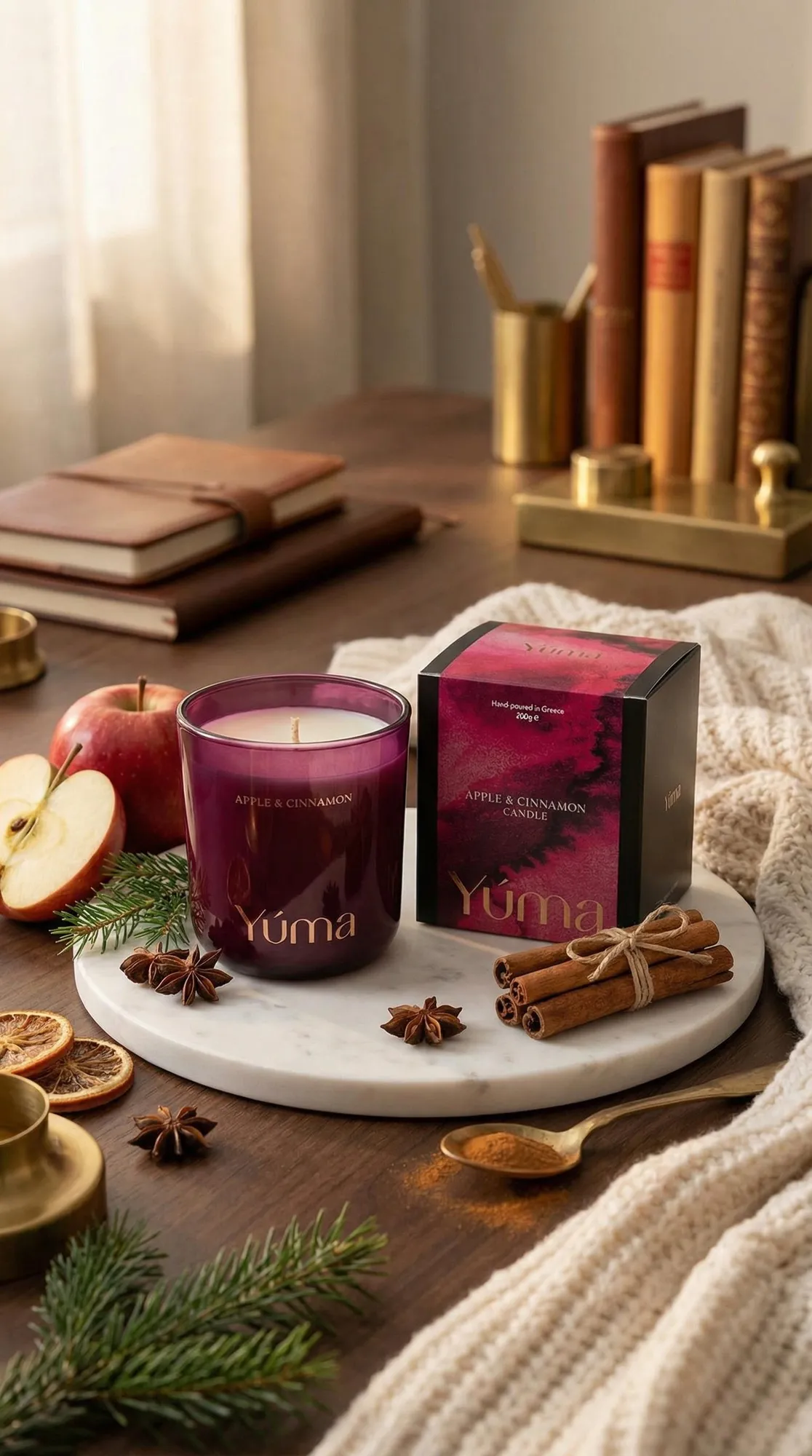 YUMA Apple Cinnamon candle in a smoky pink glass vessel beside apples and cinnamon sticks.