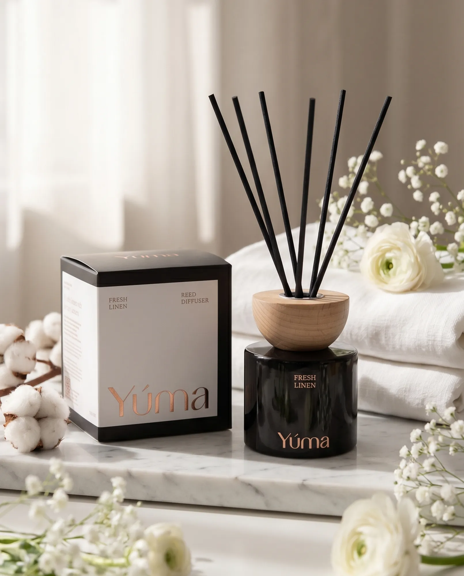 YUMA Fresh Linen reed diffuser beside white towels, cotton stems, and small white flowers.