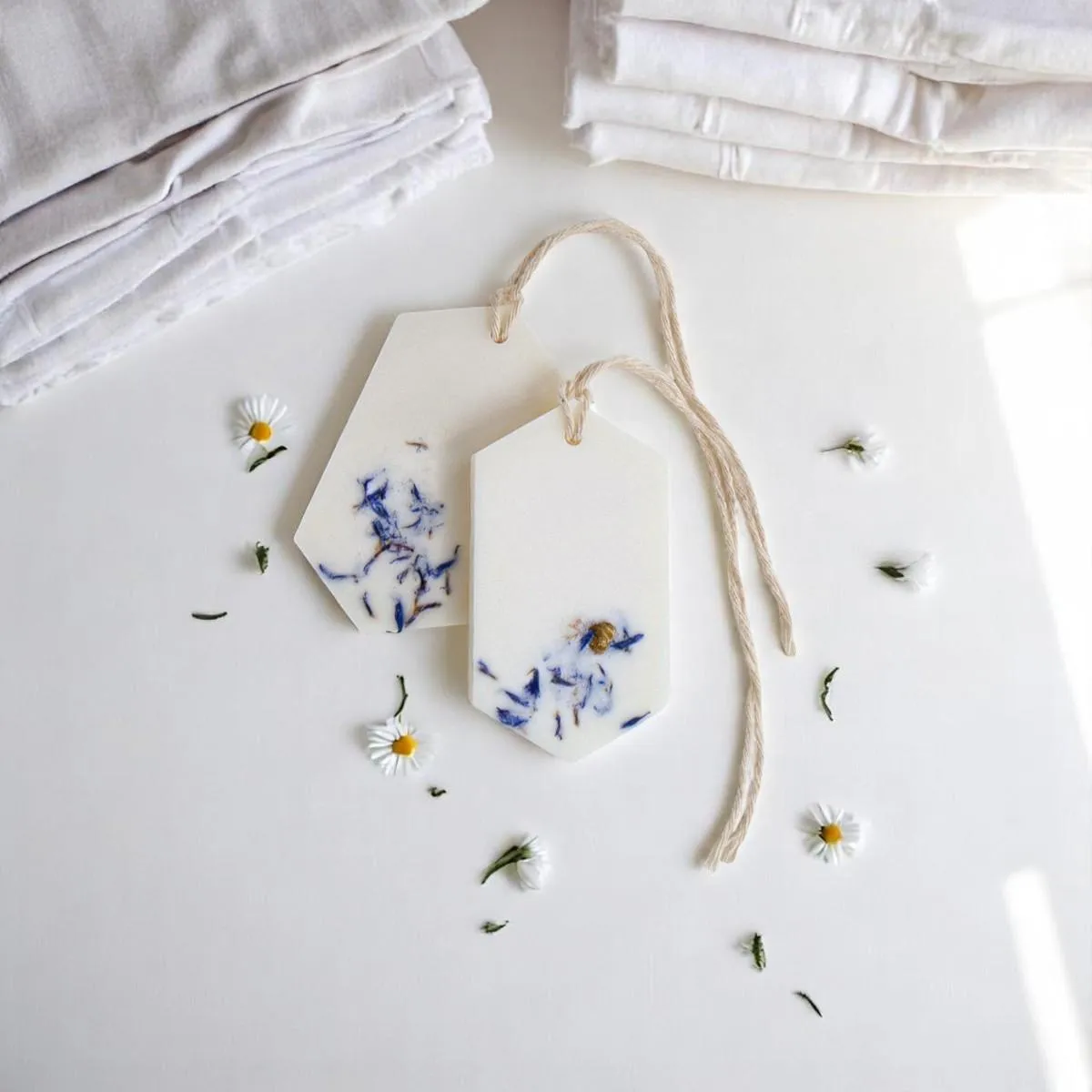 Two white Fresh Linen Wax Tablets with blue flowers beside folded fabrics.