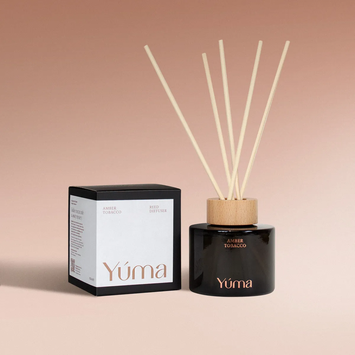 YUMA Amber Tobacco reed diffuser in a dark glass bottle beside its paper packaging.
