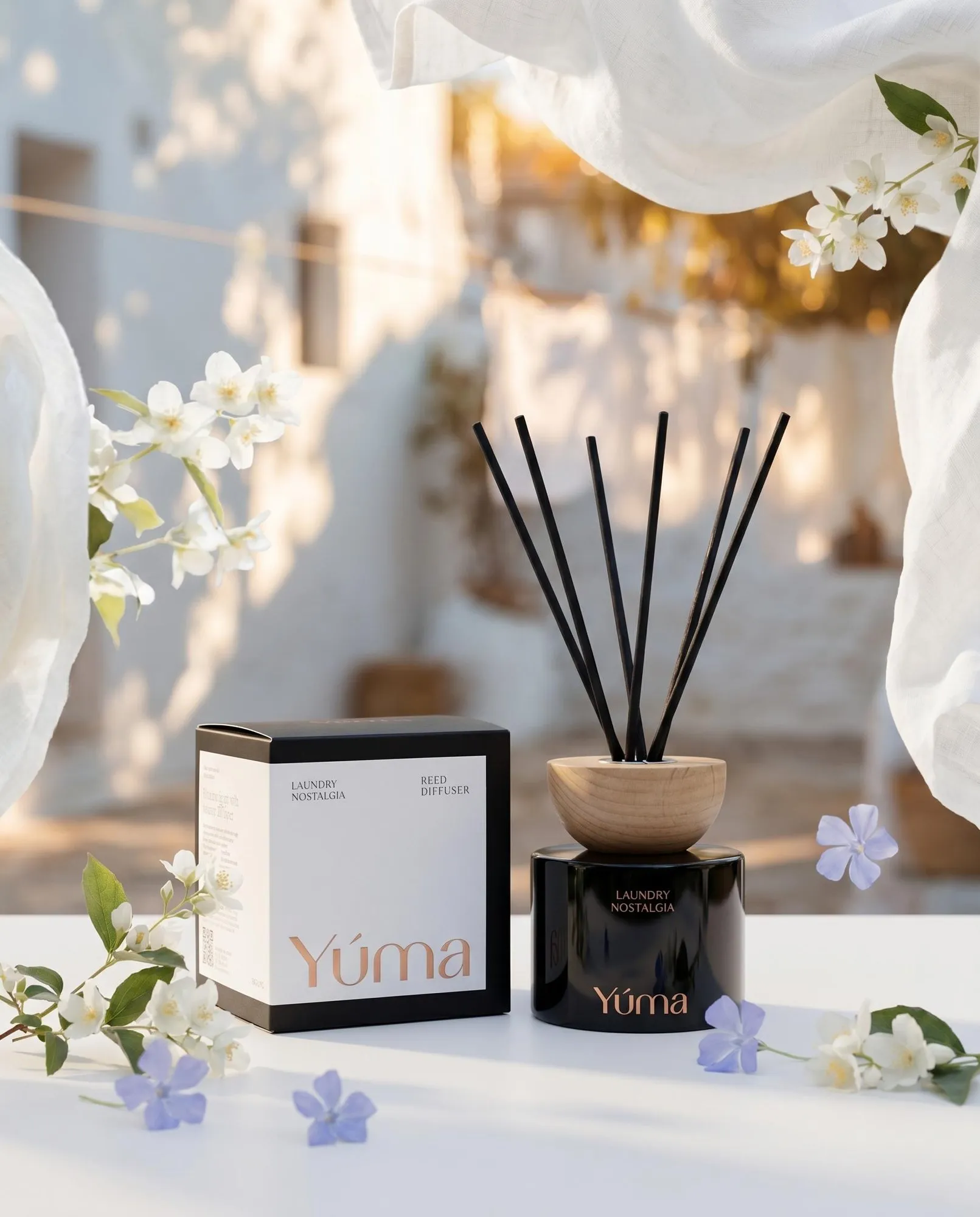 YUMA Laundry Nostalgia reed diffuser beside its packaging, surrounded by white and purple flowers.