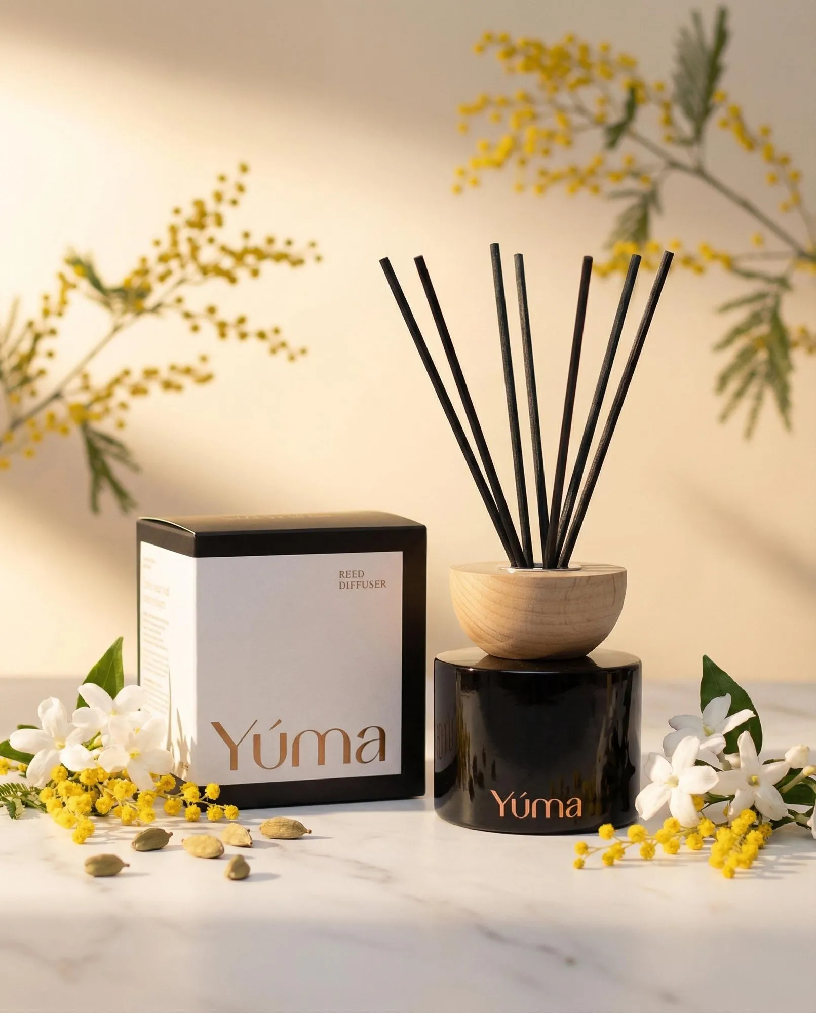 YUMA Oriental Mimosa reed diffuser placed next to white flowers and yellow mimosa blooms.