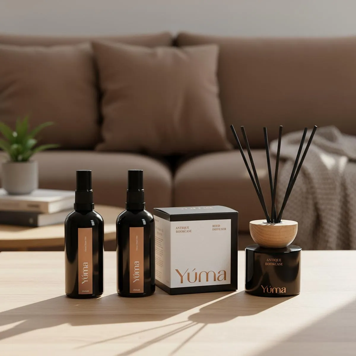 Two room sprays, a box, and a YUMA Antique Bookcase reed diffuser on a wooden table.