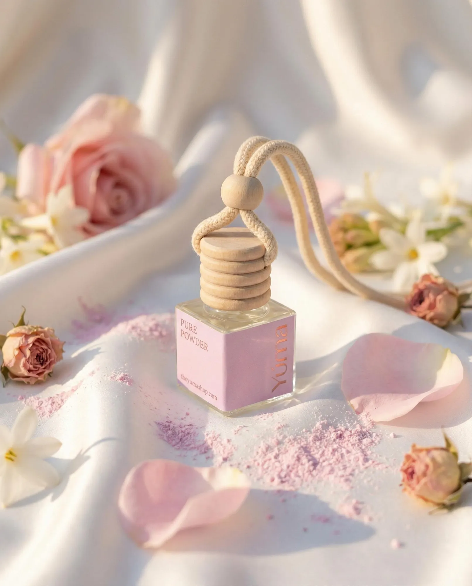 YUMA Pure Powder car diffuser on white fabric with pink petals and blossoms.