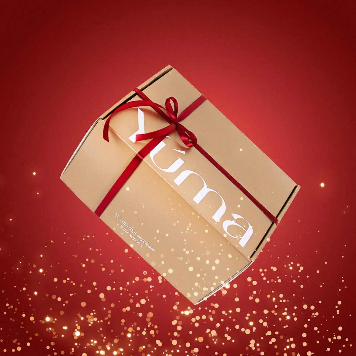 YUMA paper gift box with a red ribbon on a red background with gold shimmer.