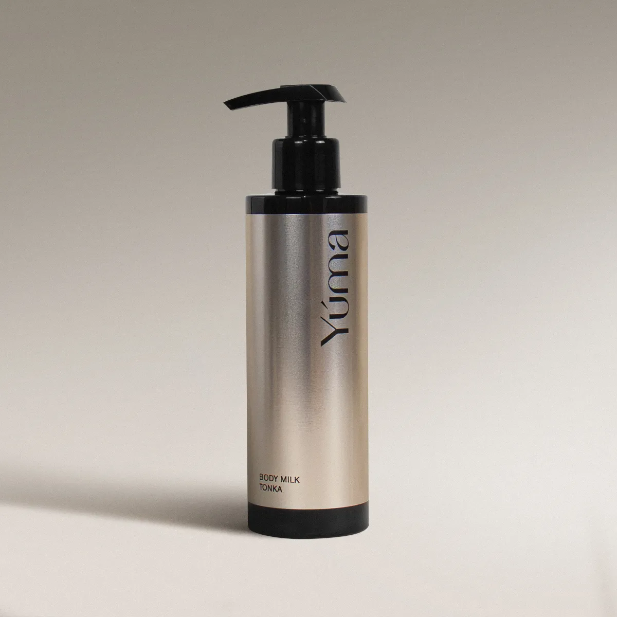 YUMA Tonka Body Milk in a metallic bottle with a black pump, on a neutral background.