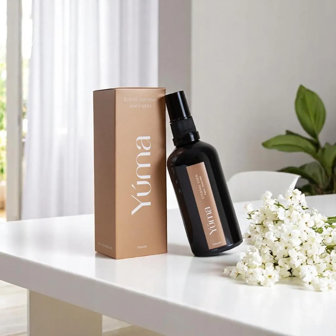 YUMA Eternal Eden room spray in a dark bottle beside its packaging and white flowers.