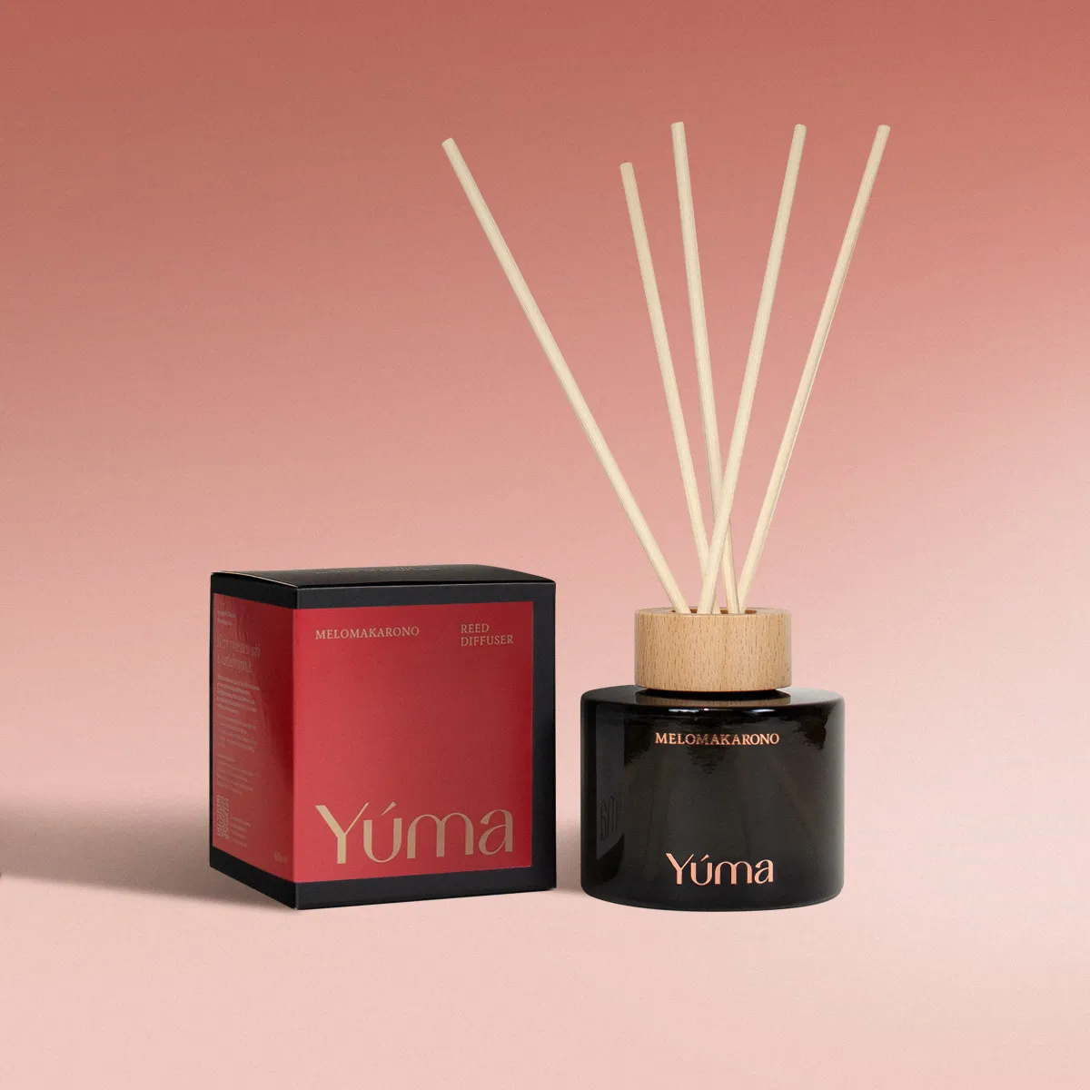 YUMA Melomakarono reed diffuser in a black glass vessel next to its red packaging.