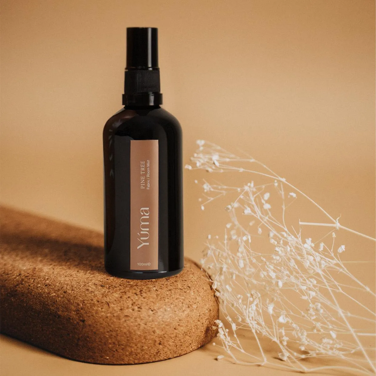 Dark glass YUMA Pine Tree bottle on a cork surface next to white dried flowers.