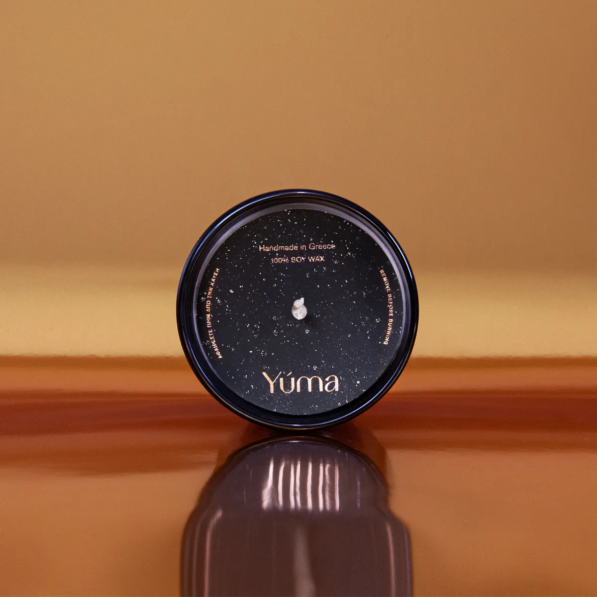 Top view of a YUMA Black Orchid candle with a black cover on a warm-toned background.