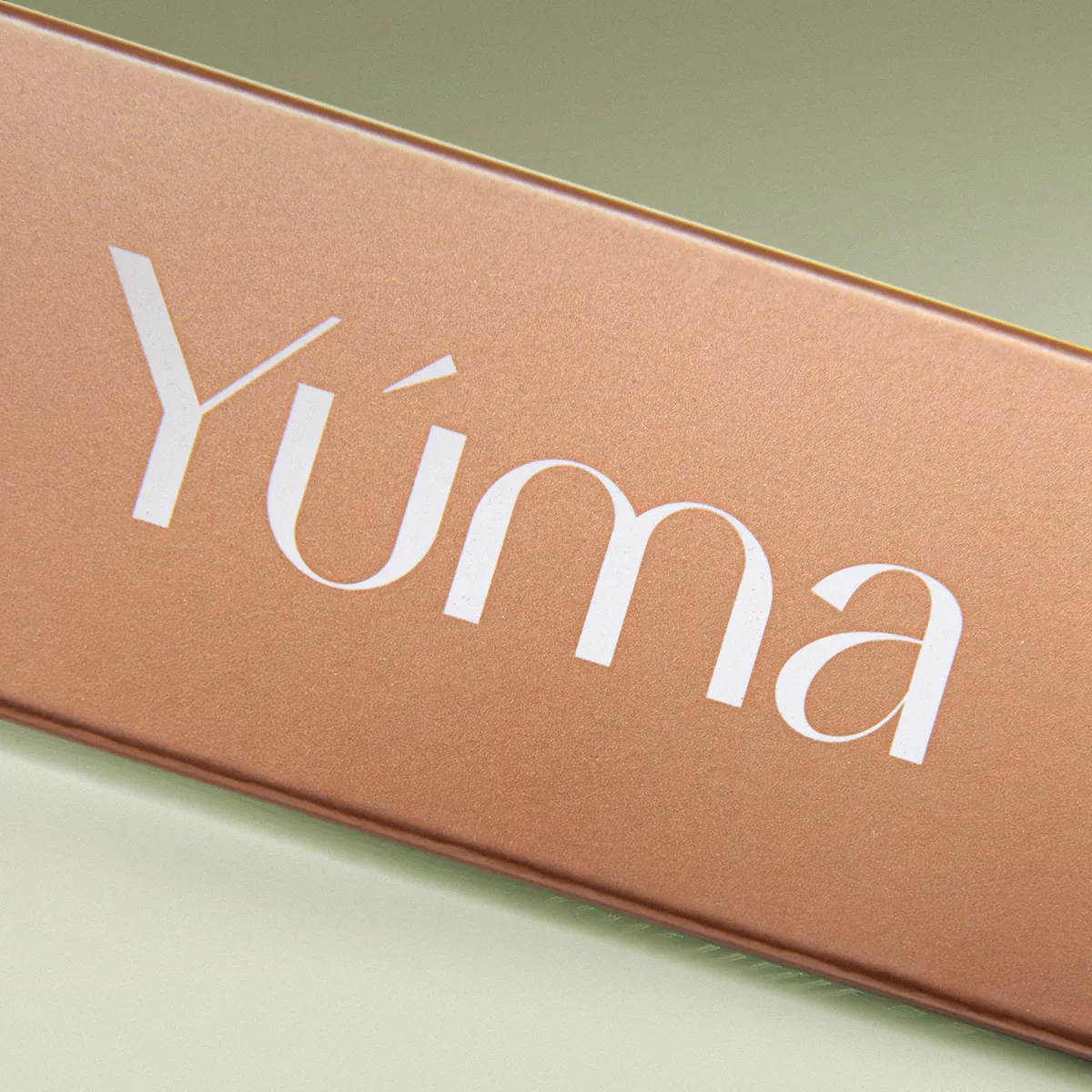 Close-up of the YUMA logo in white lettering on a copper-toned metallic surface.