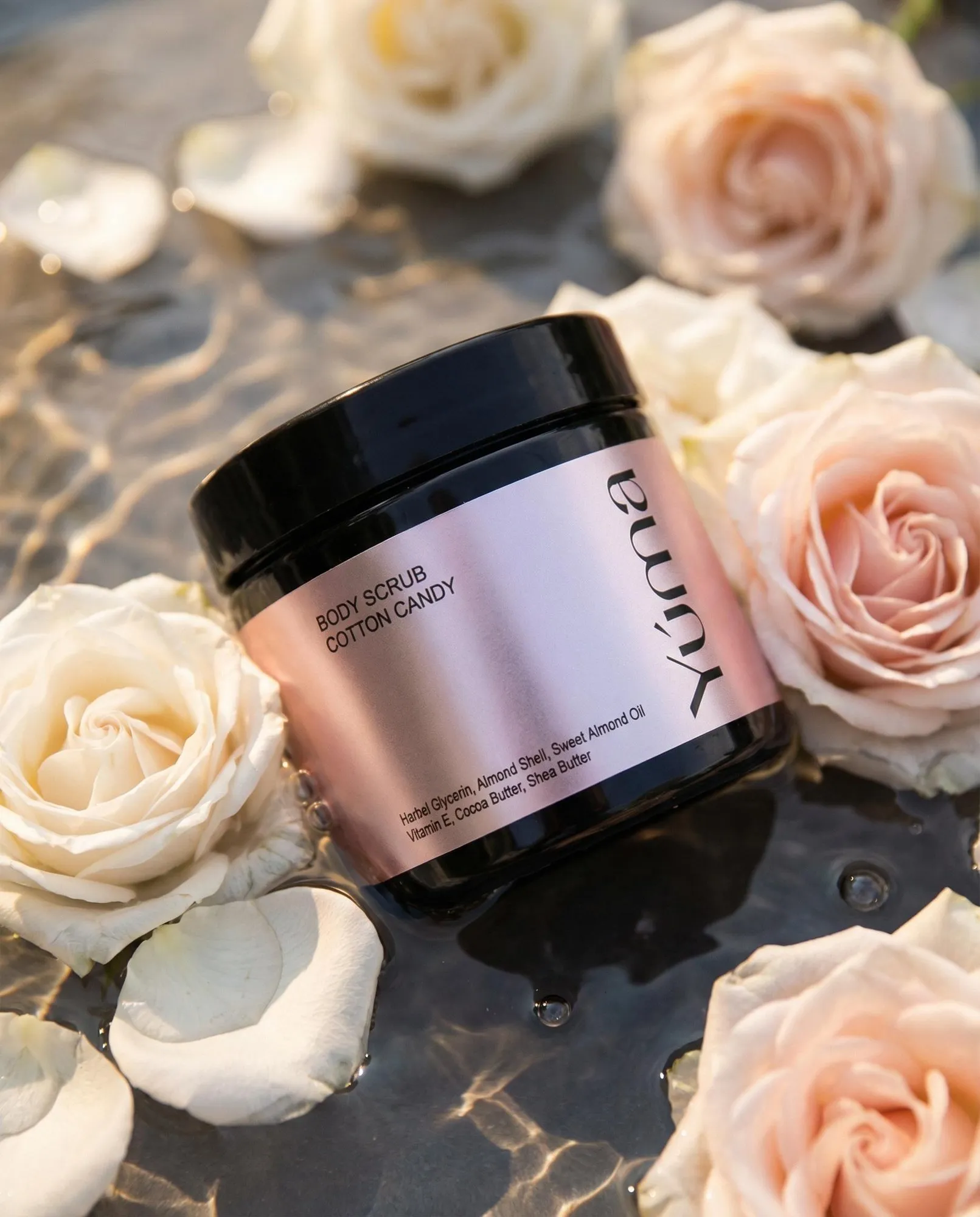 YUMA Cotton Candy Body Scrub in pink packaging, submerged in water with pale roses.