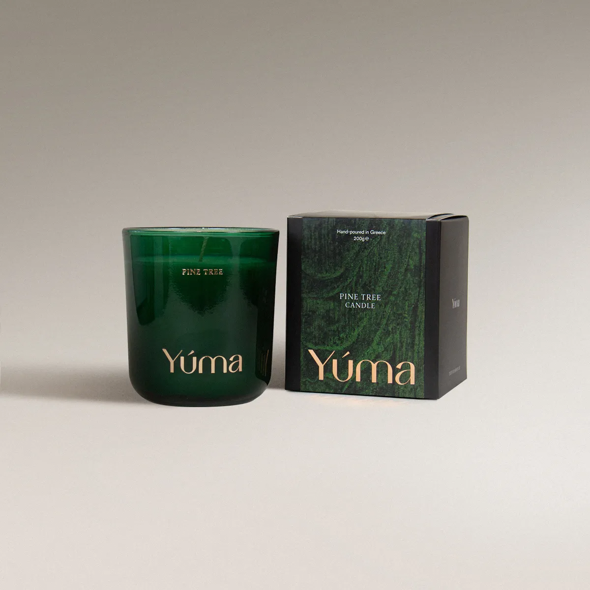 YUMA Pine Tree candle in a green glass vessel beside its paper packaging on a grey background.