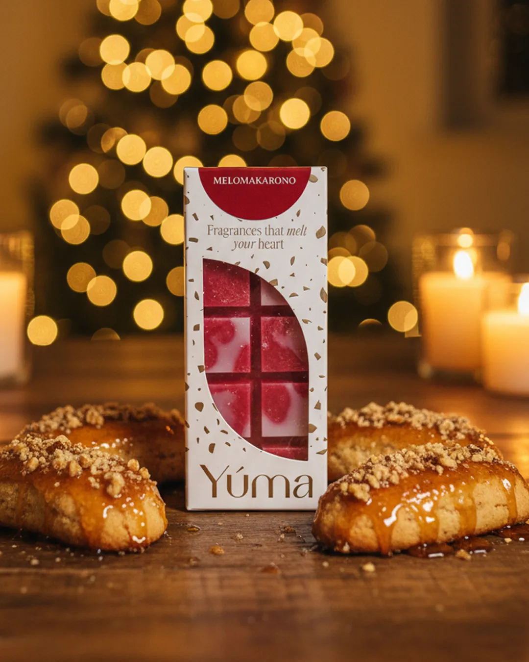 YUMA Melomakarono wax melts packaging surrounded by melomakarona cookies, with Christmas lights and candles in the background.