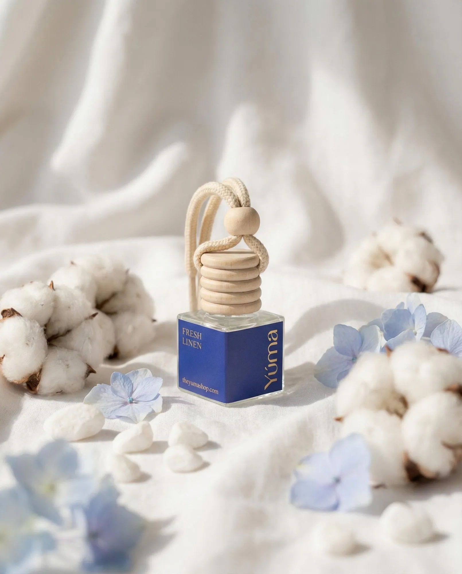 YUMA Fresh Linen Car Diffuser surrounded by cotton flowers and blue blooms.