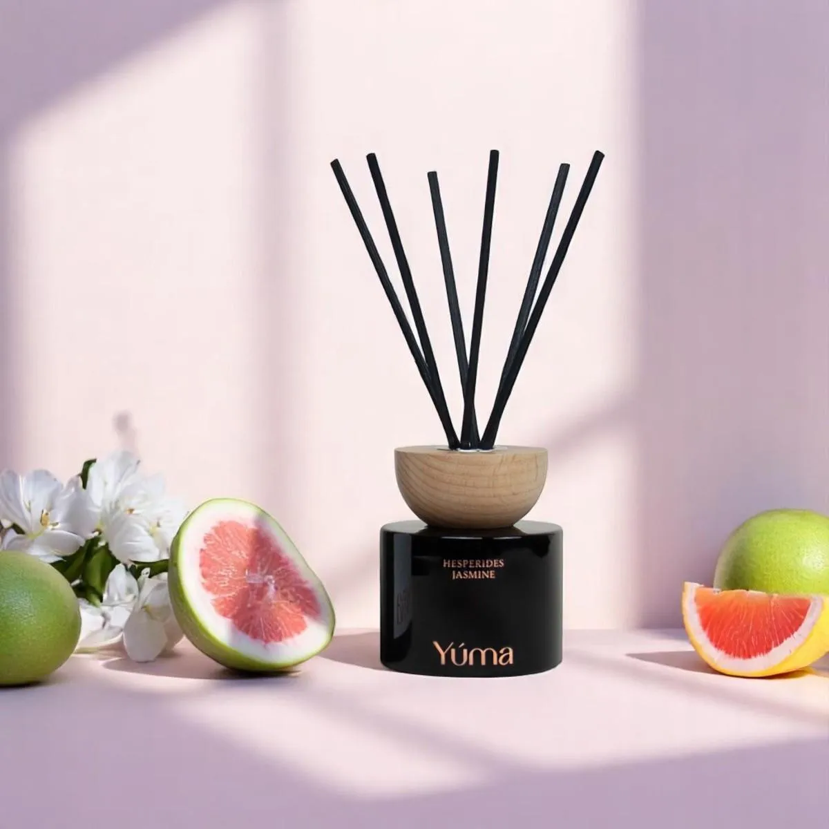 YUMA Hesperides Jasmine reed diffuser with black sticks, surrounded by sliced grapefruit and white blossoms.