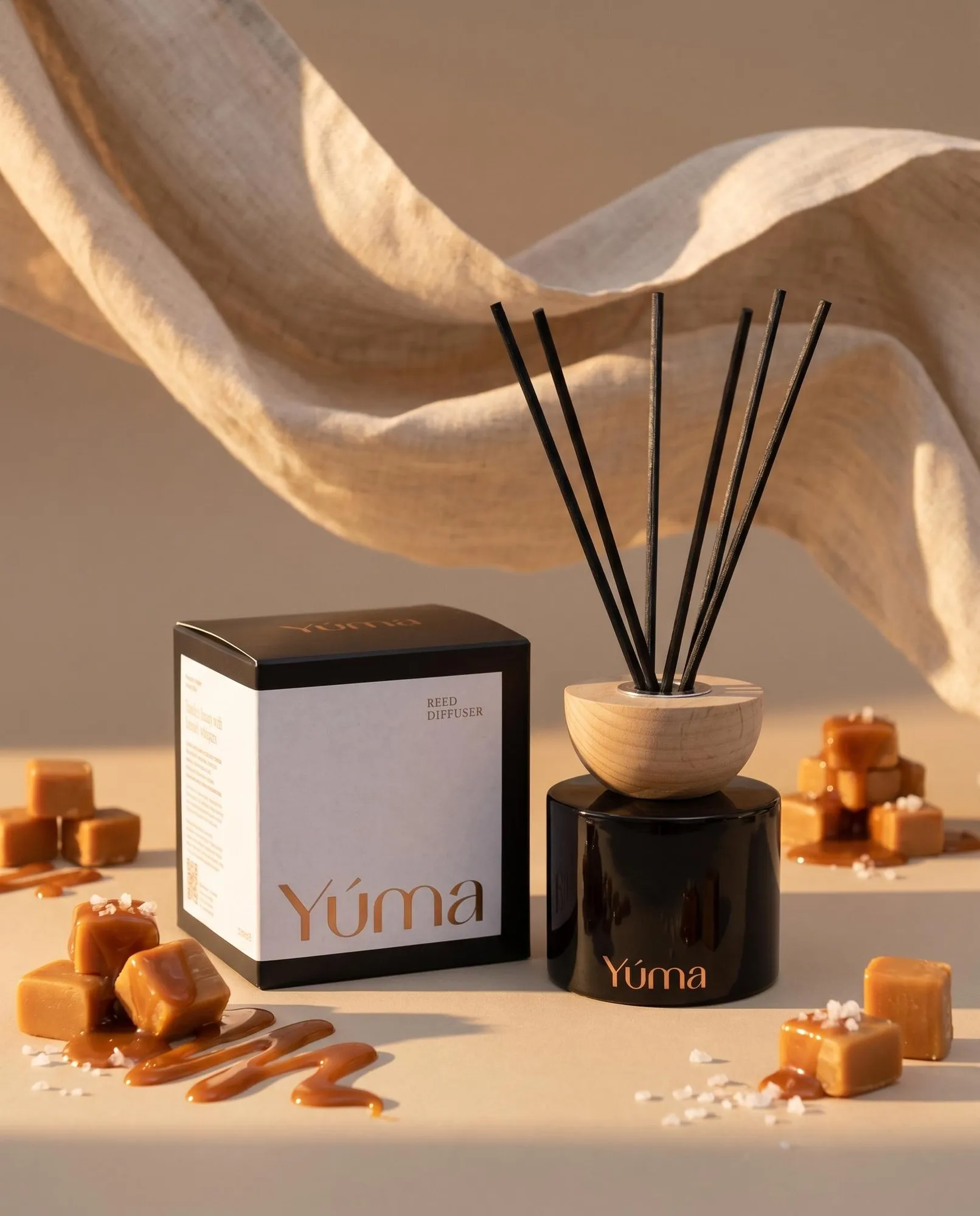 YUMA Salted Caramel reed diffuser placed next to caramel cubes and coarse salt.