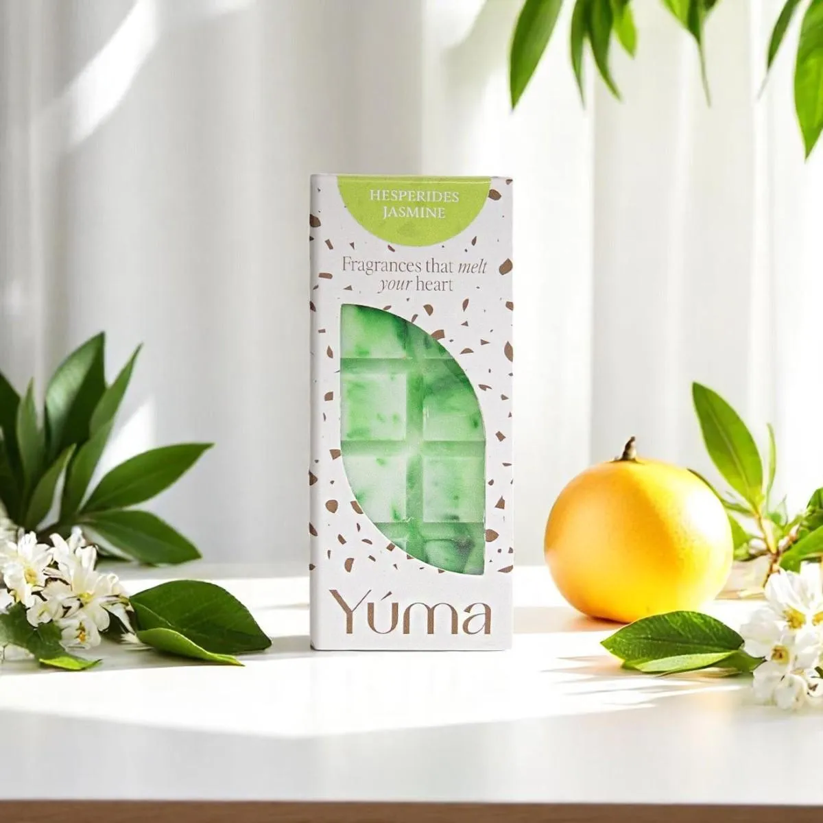 YUMA Hesperides Jasmine green wax melt bar next to a citrus fruit and white blossoms.