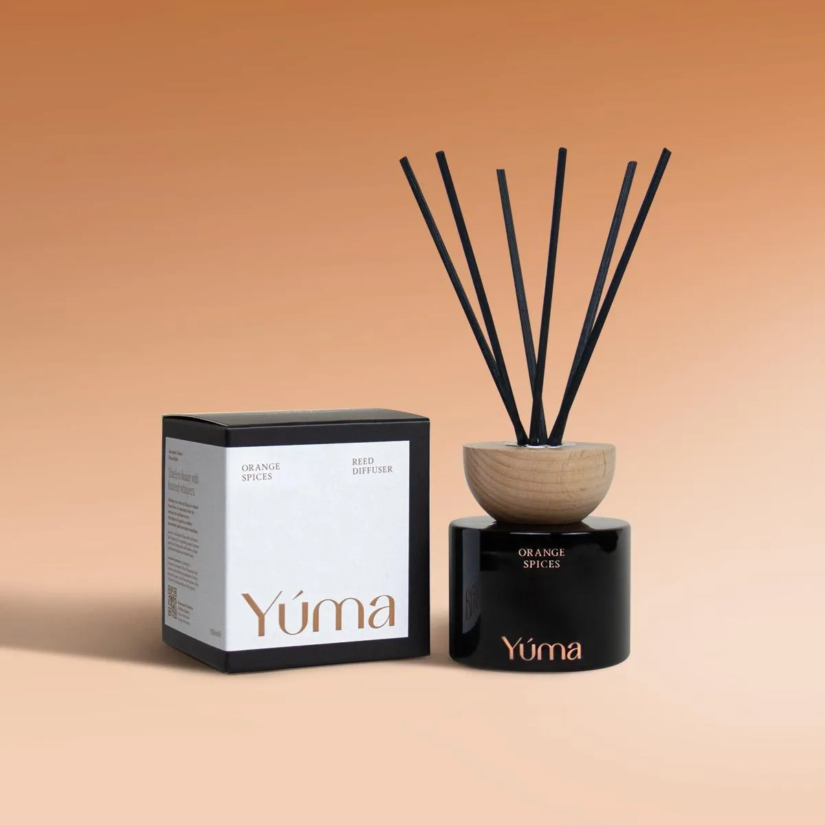 YUMA Orange Spices reed diffuser in a black glass bottle next to its packaging.