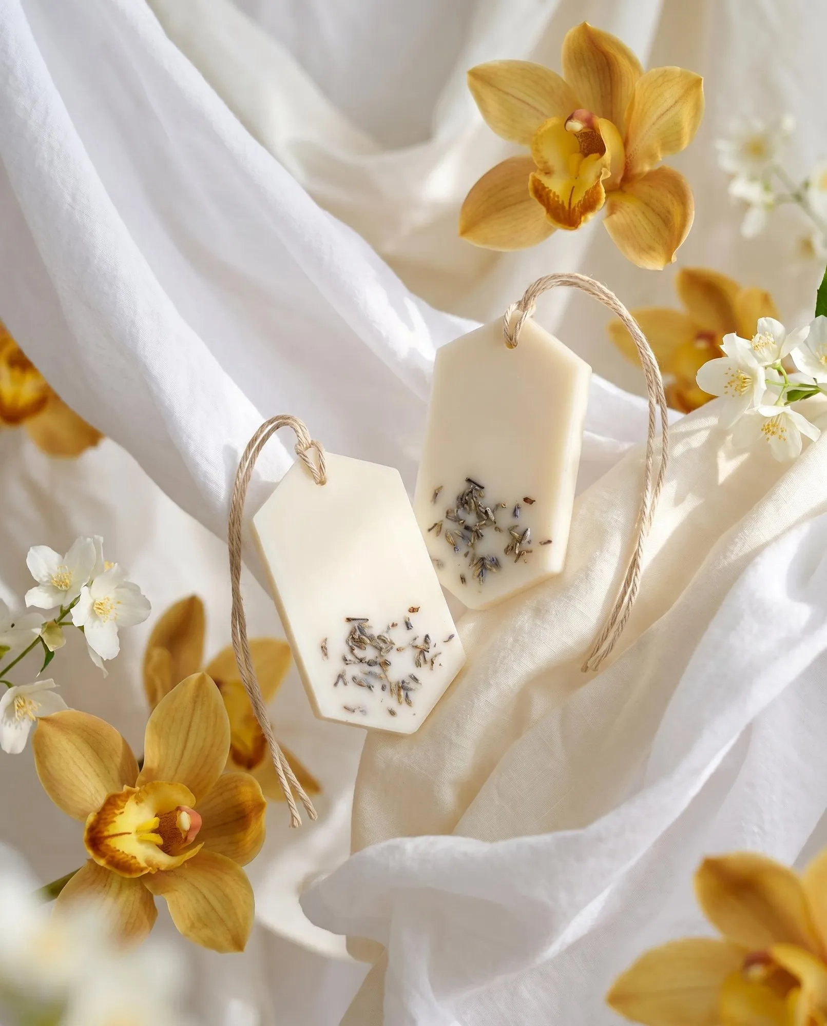 Two Gold Orchid Wax Tablets hanging among white fabrics and yellow orchids.