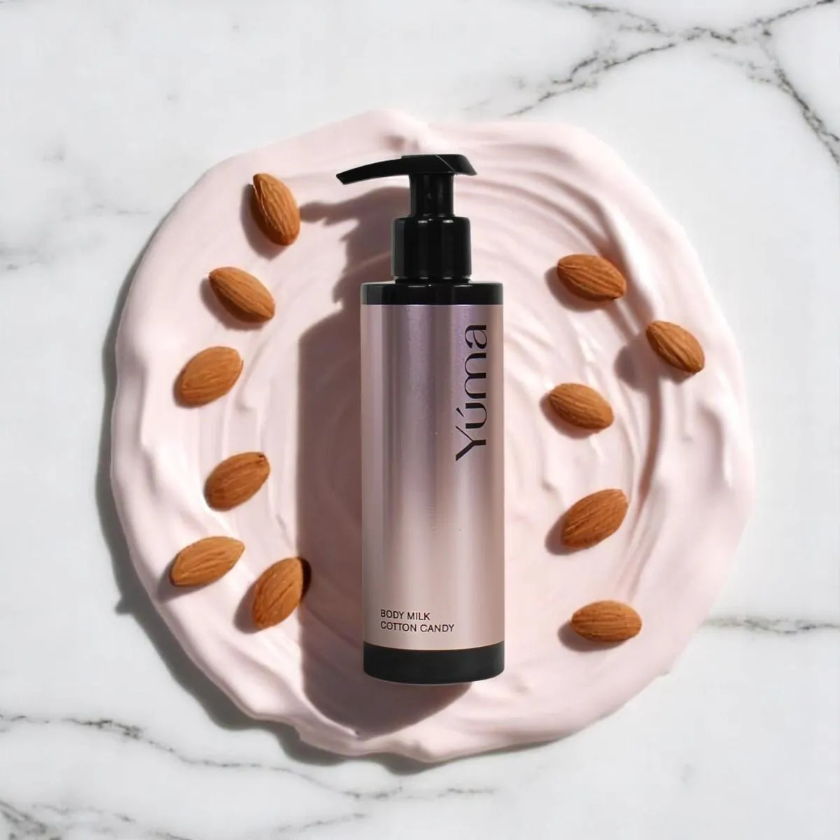 YUMA Cotton Candy Body Milk on a pink cream texture with almonds on a marble surface.
