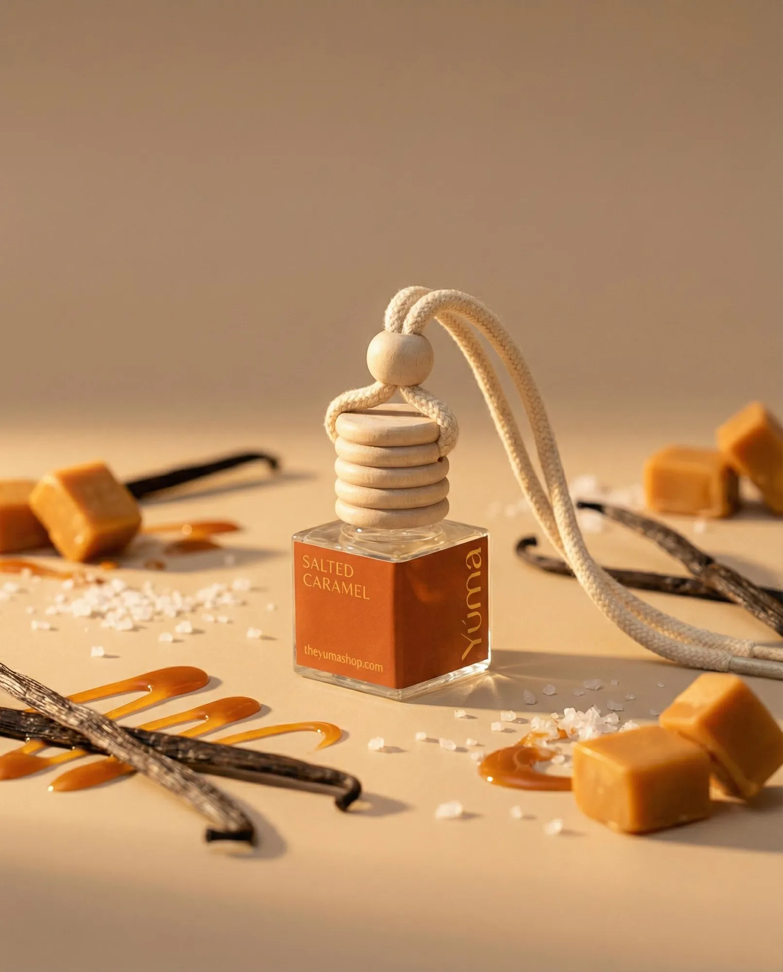 YUMA Salted Caramel car diffuser surrounded by caramel cubes, salt crystals, and vanilla sticks.