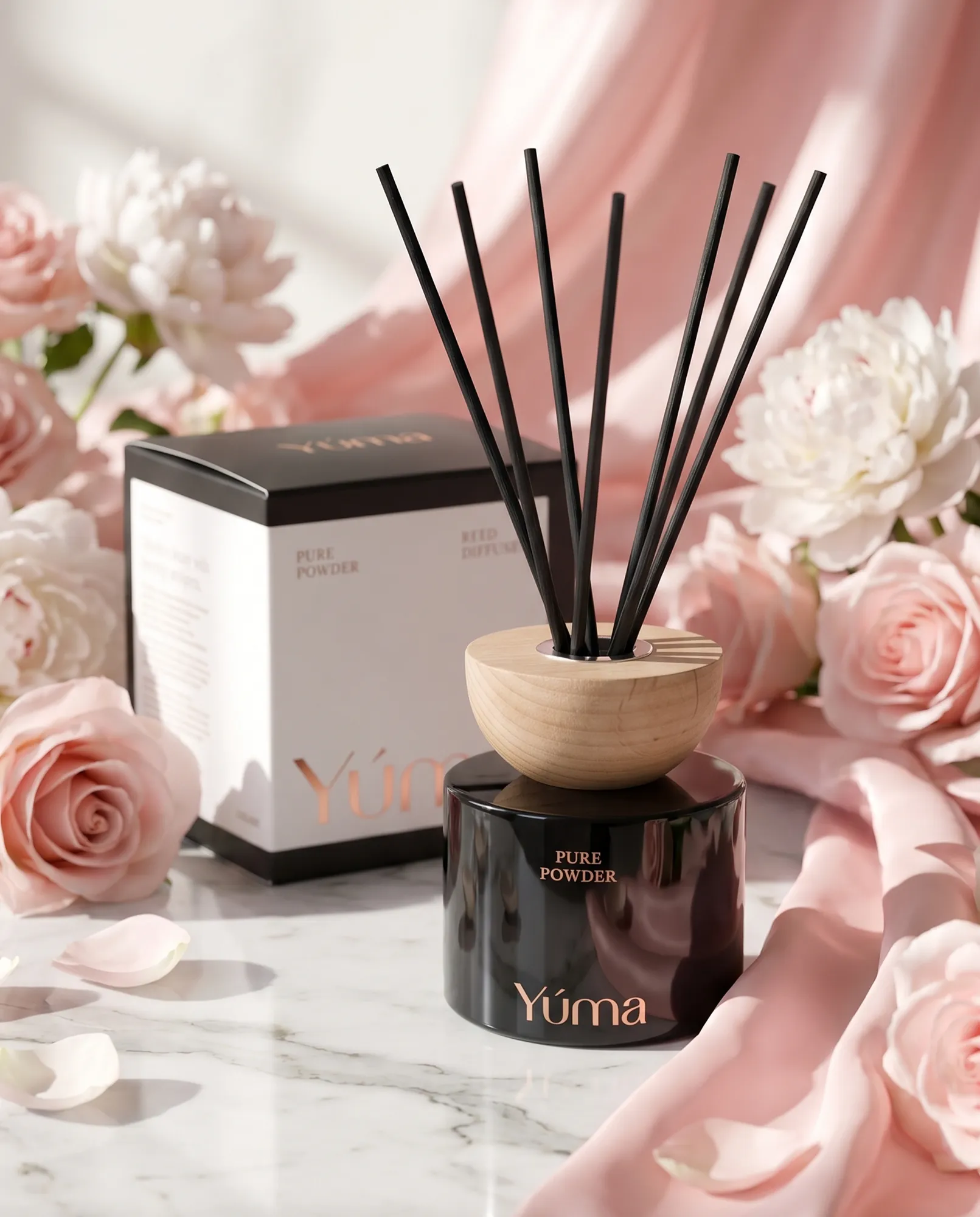 YUMA Pure Powder Reed Diffuser in a black glass vessel, nestled among pink roses and soft fabrics.