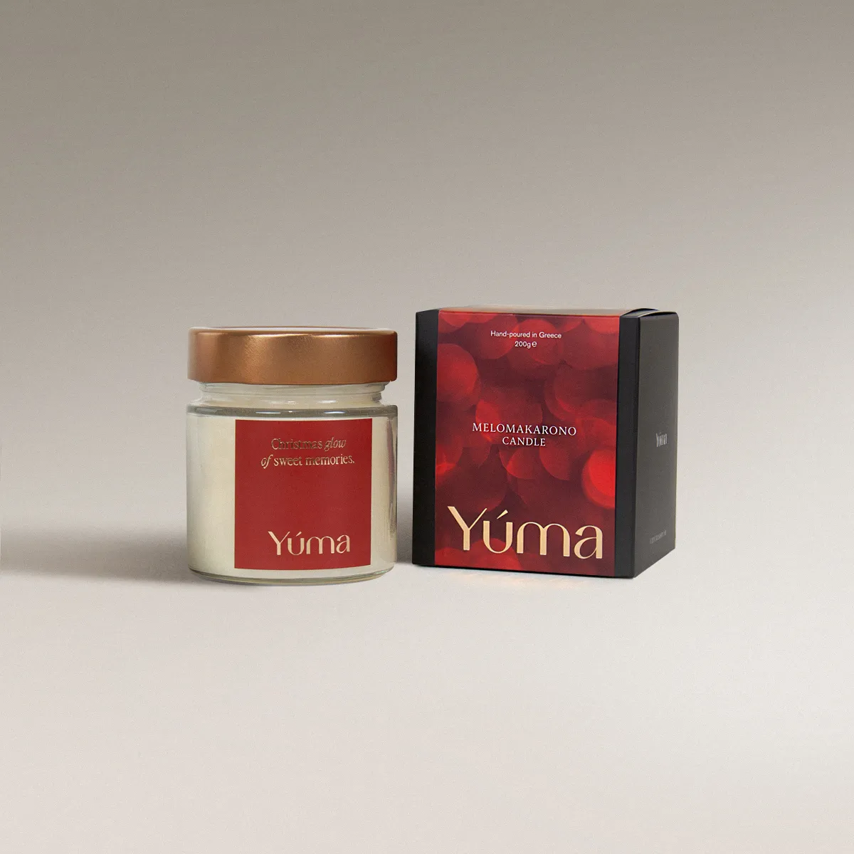 YUMA Melomakarono candle in a glass vessel with a copper-toned lid beside its red packaging.