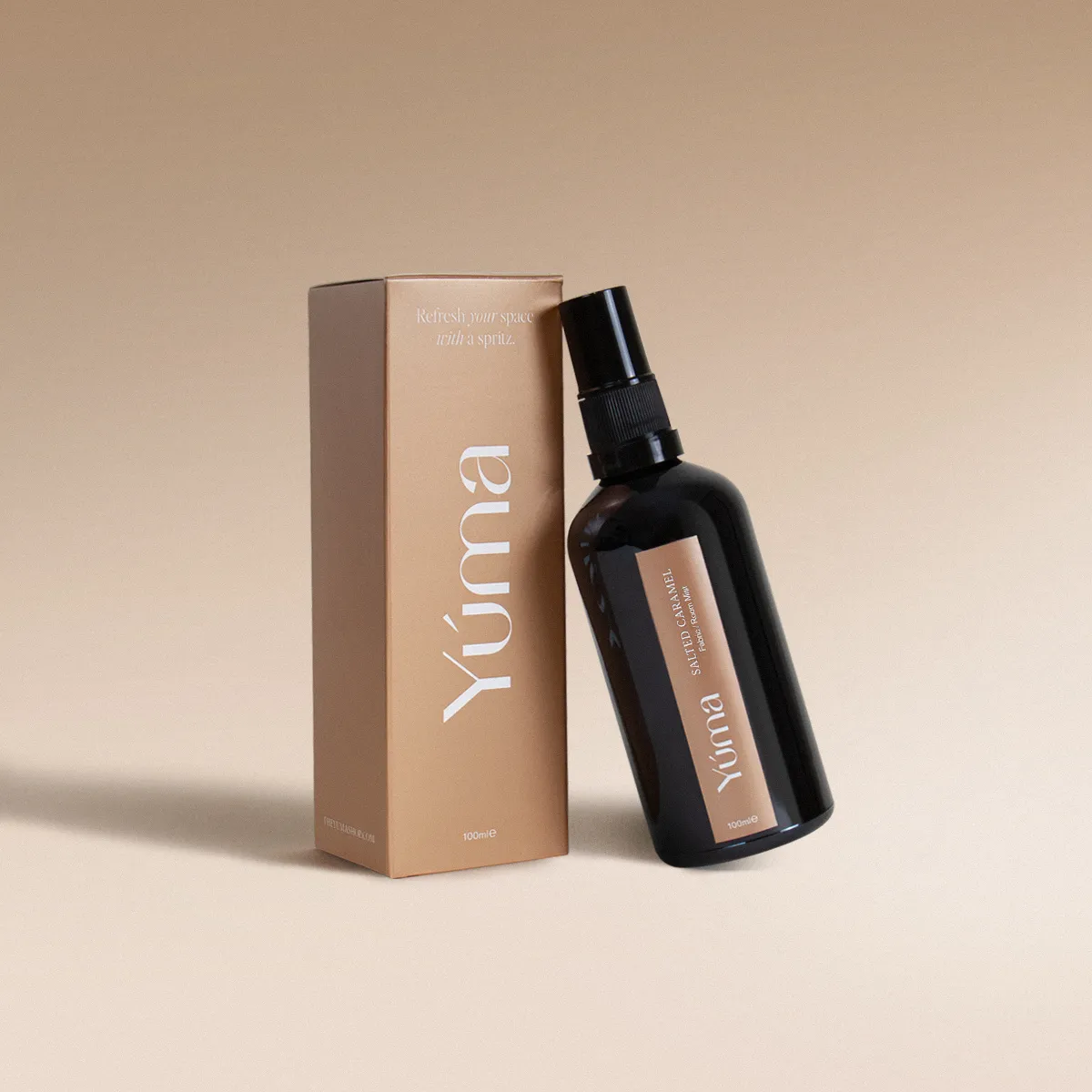 YUMA Salted Caramel Fabric Mist in a dark glass bottle next to its beige paper packaging.
