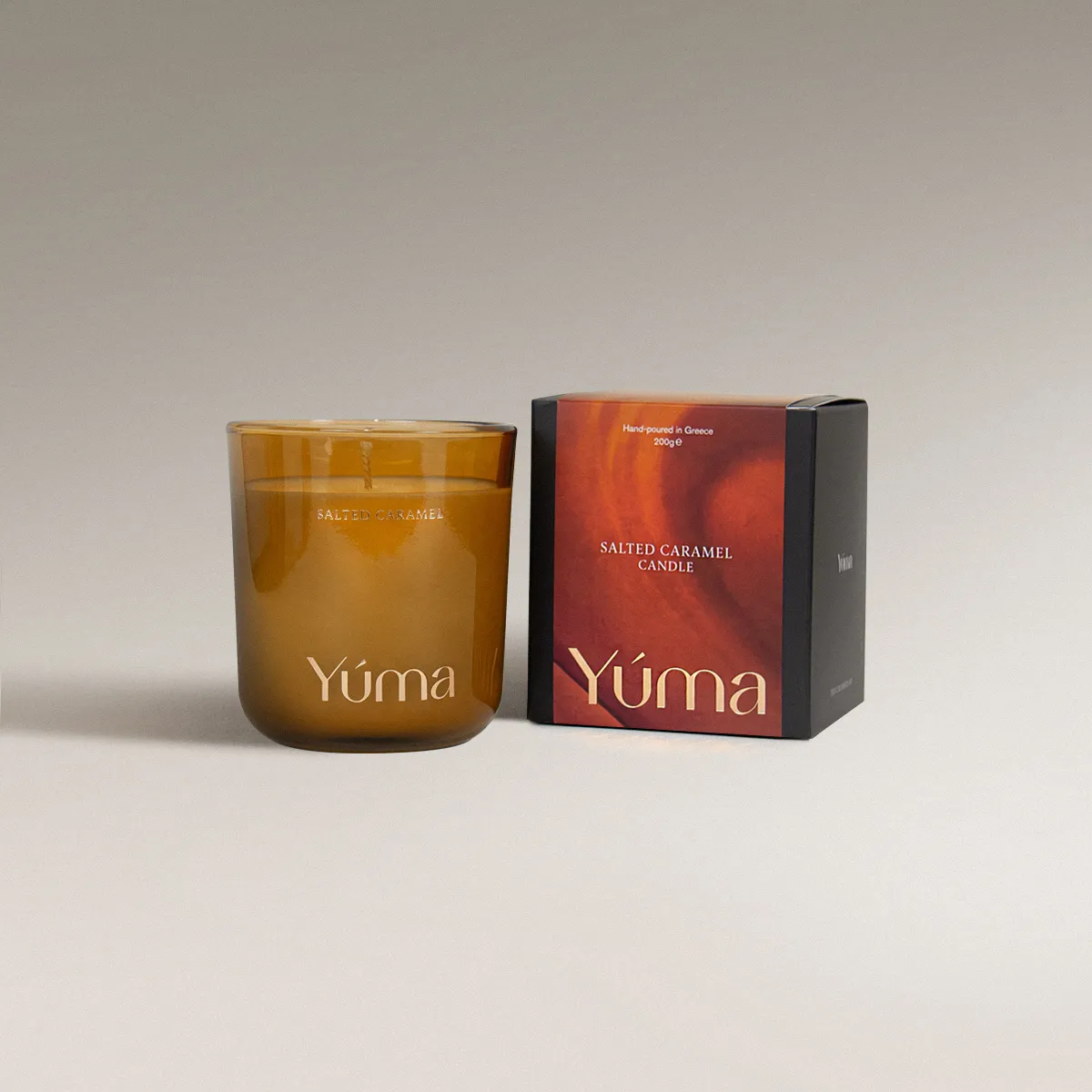 YUMA Salted Caramel candle in an amber glass vessel beside its paper packaging.