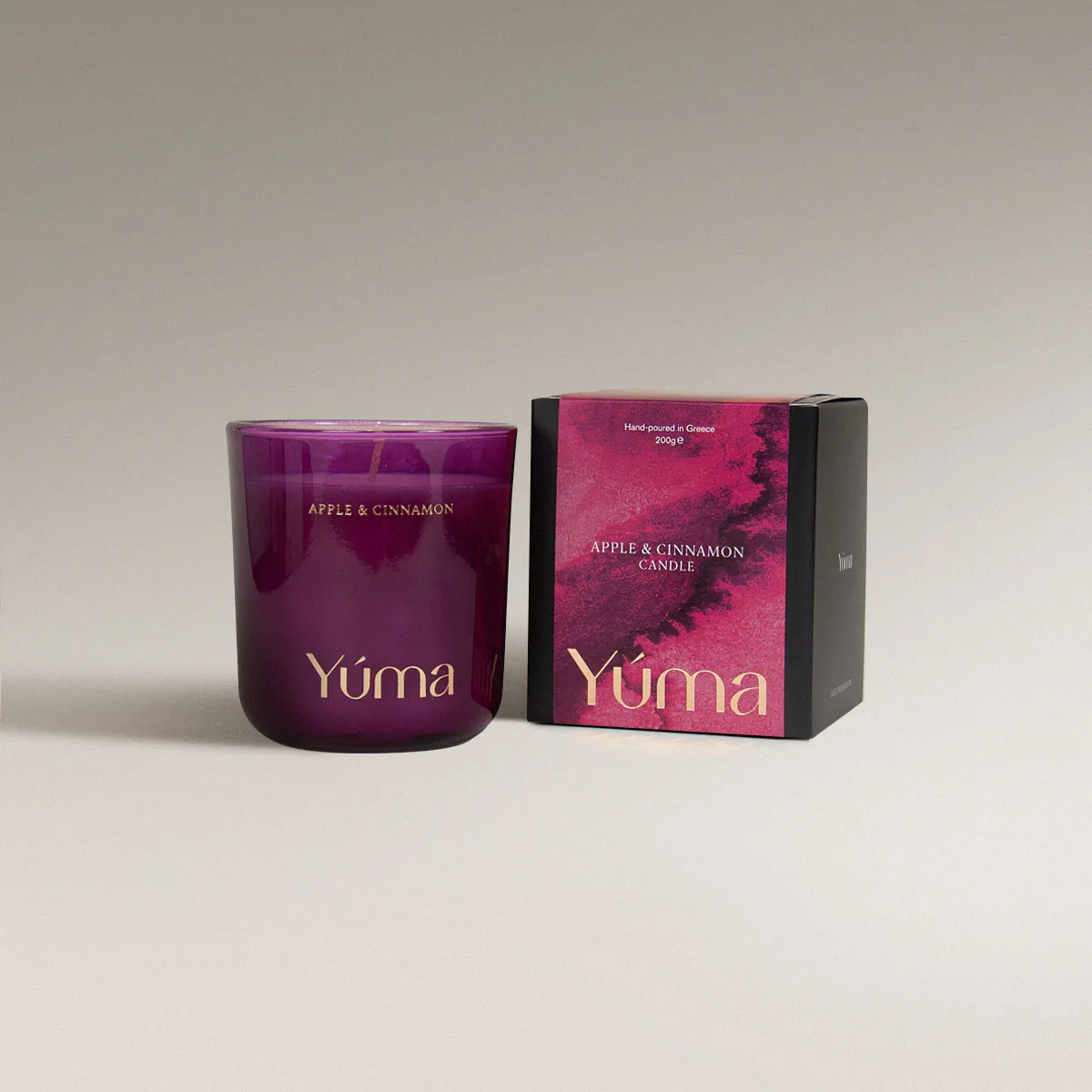 YUMA Apple Cinnamon candle in a smoky pink glass vessel beside its paper packaging.