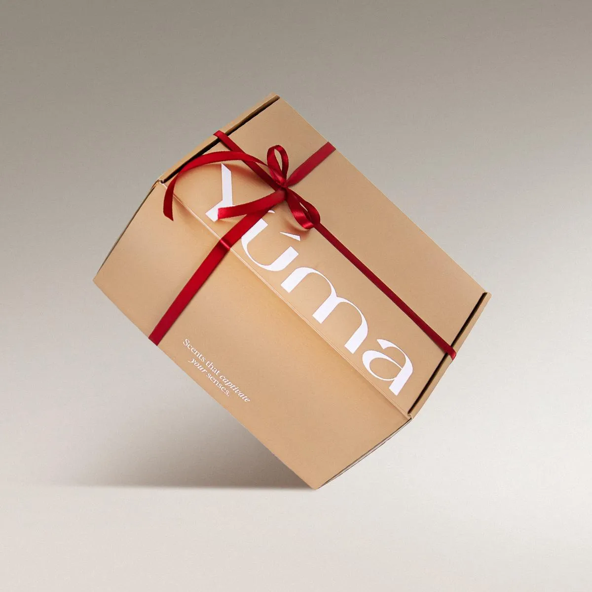 Closed kraft-paper YUMA Gift Set box with a red ribbon and bow on a grey background.