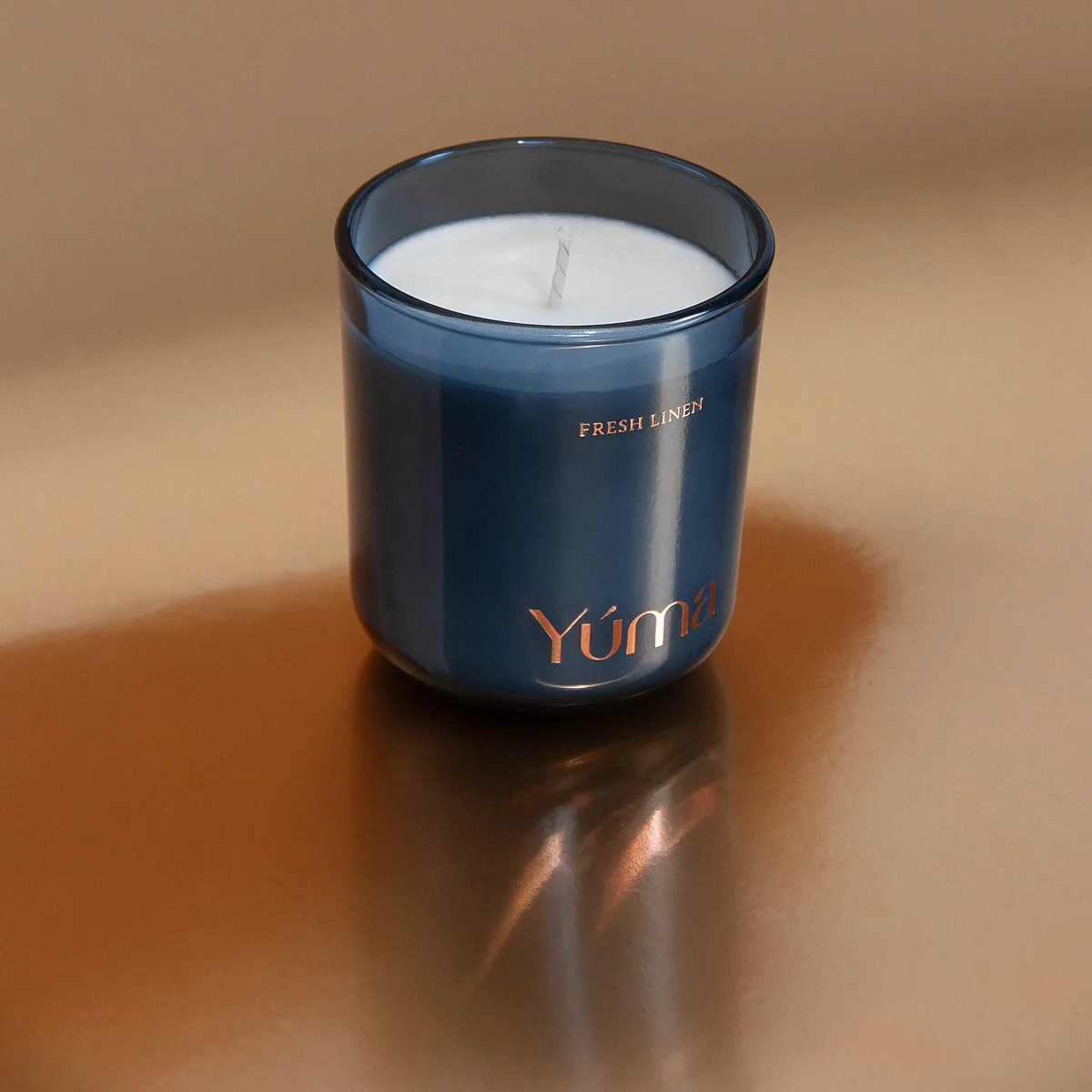 YUMA Fresh Linen candle in a blue glass vessel on a glossy brown surface.