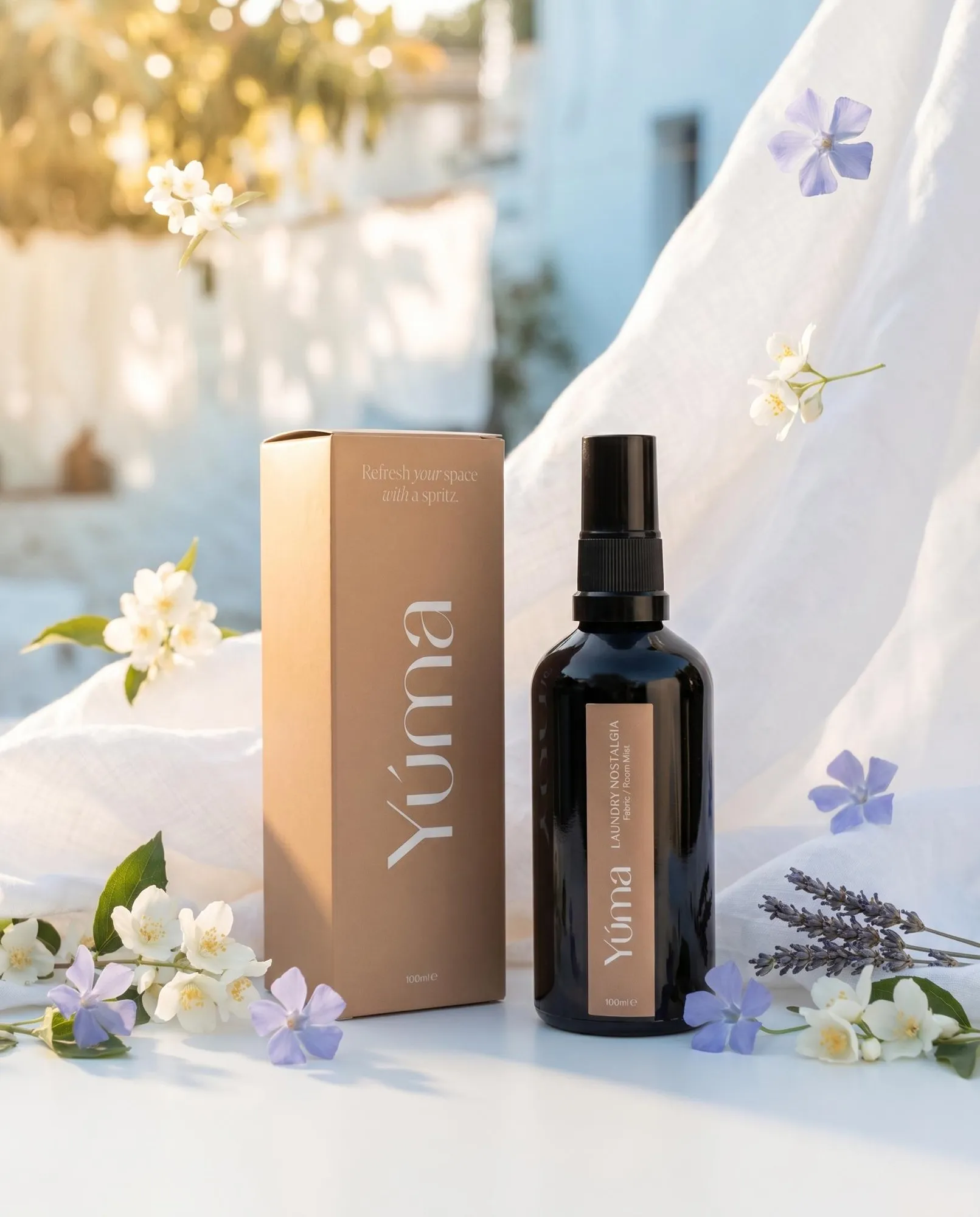 YUMA Laundry Nostalgia fabric mist next to its packaging, surrounded by white and purple flowers.