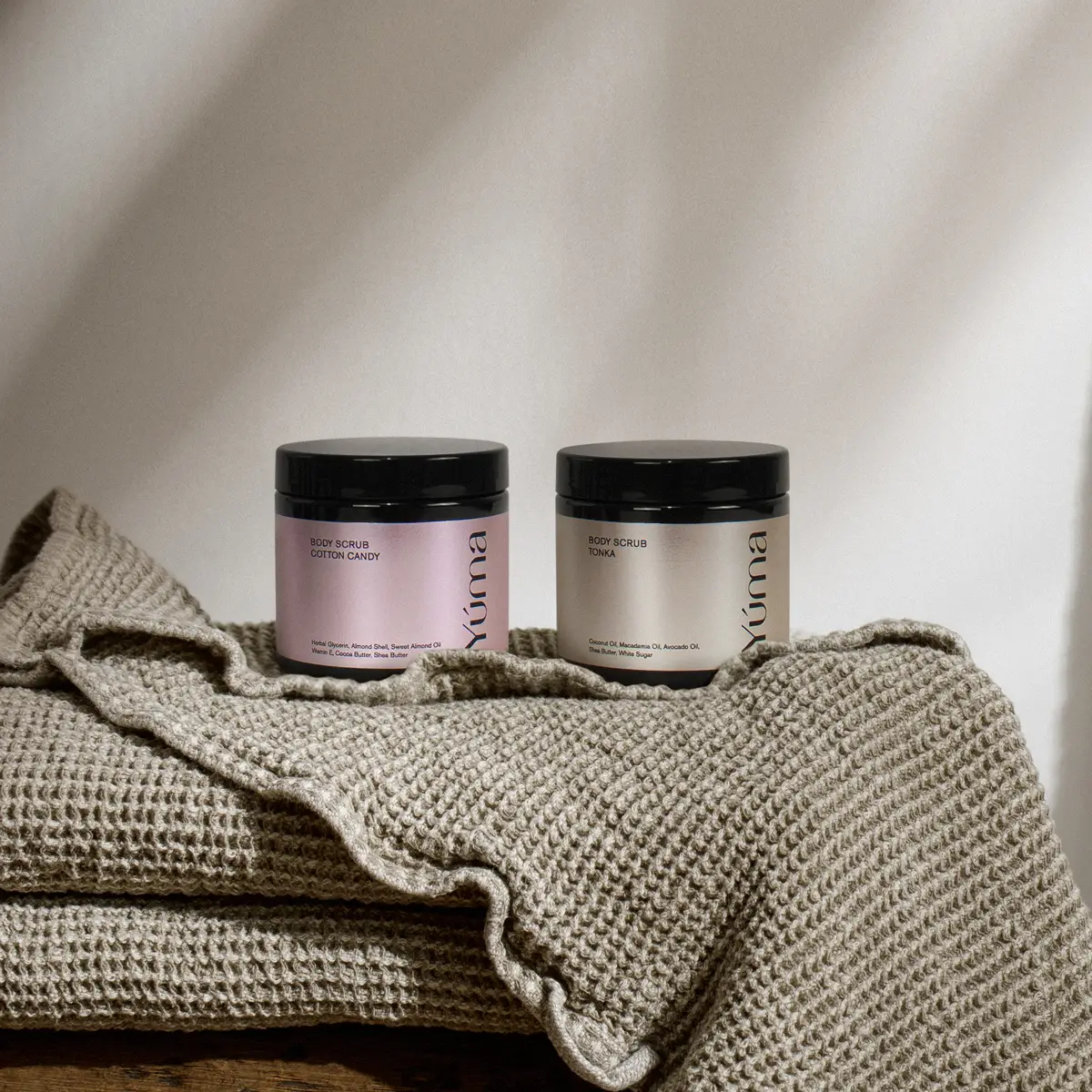 Two YUMA body scrub jars, Cotton Candy and Tonka, on a waffle-knit towel Two YUMA body scrub jars, Cotton Candy and Tonka, on a waffle-knit towel