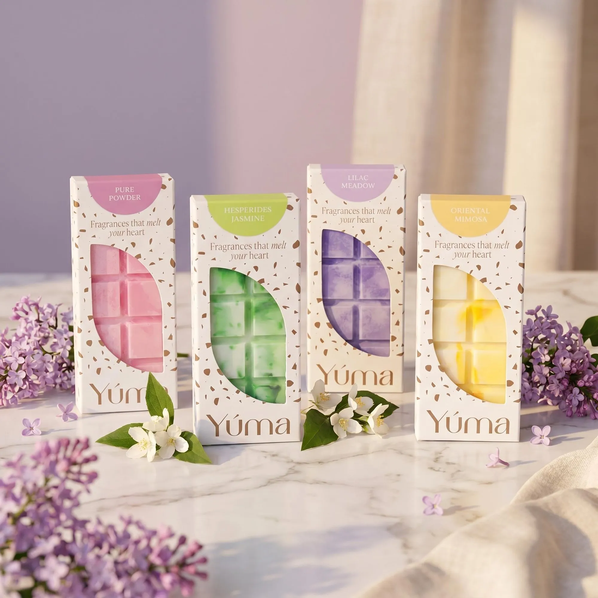 Signature Collection - Wax Melt Set Four YUMA wax melts in paper packaging on marble, surrounded by lilac and jasmine blossoms.